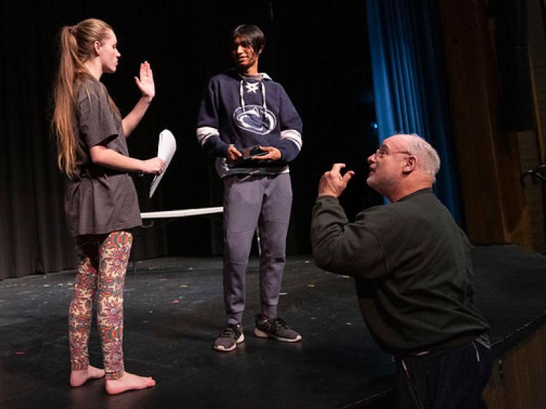 Students run lines on stage with professor in a theatre class