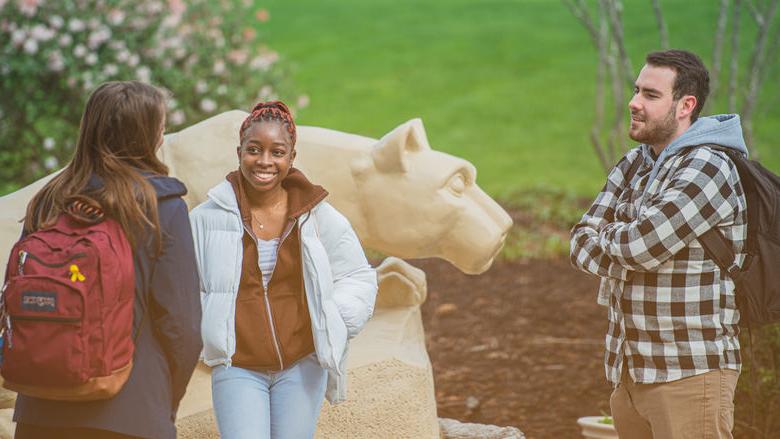 Three students around the Nittany Lion Shrine